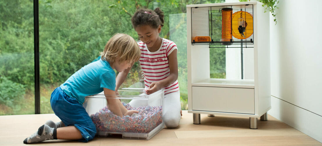 Twee kinderen spelen met een hamster naast een Qute hamsterkooi