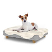 Hond zittend op een klein Topology hondenbed met schapenvacht topper en houten ronde poten