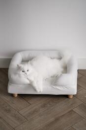 Een witte kat geniet van het comfort van zijn witte bolster bed