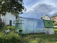 Een kippenhok en een ren met handgrepen aan het uiteinde van de ren, overdekt met doorzichtige dekzeilen