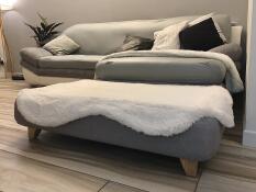 Een grijs bed met een witte schapenvacht topper en vierkante houten poten