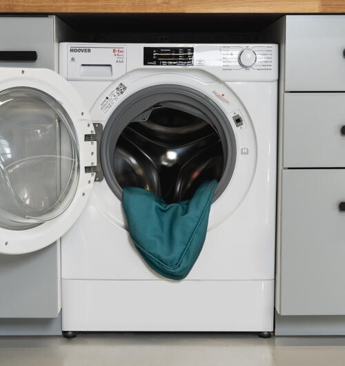 Wasmachine met Geopende deur en bolsterbedovertrek met sparrenprint aan de binnenkant.