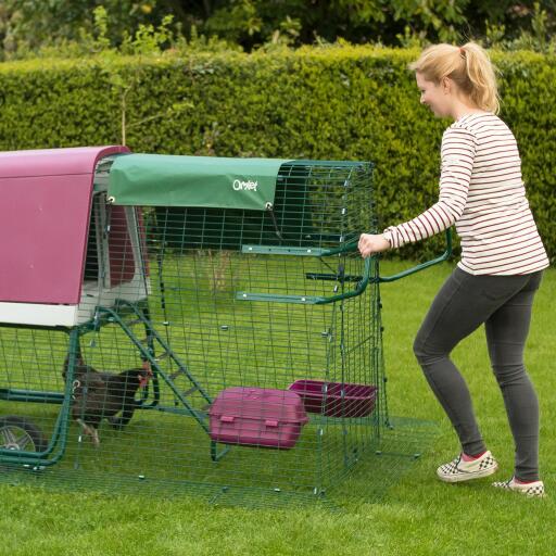 Vrouw die Eglu Go verplaatst kippenhok met wielen en ren handgrepen