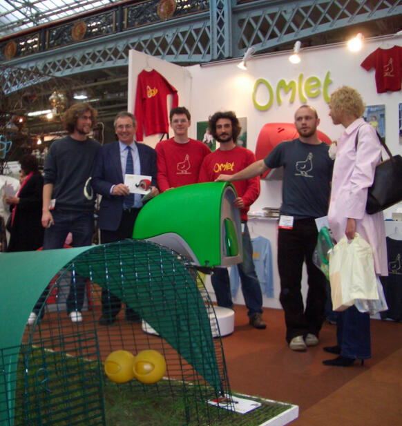 Een groep mensen poseert bij een stand met het Eglu Cube kippenhok