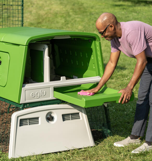 Een man die de mestbak van het kippenhok Eglu Cube schoonmaakt.