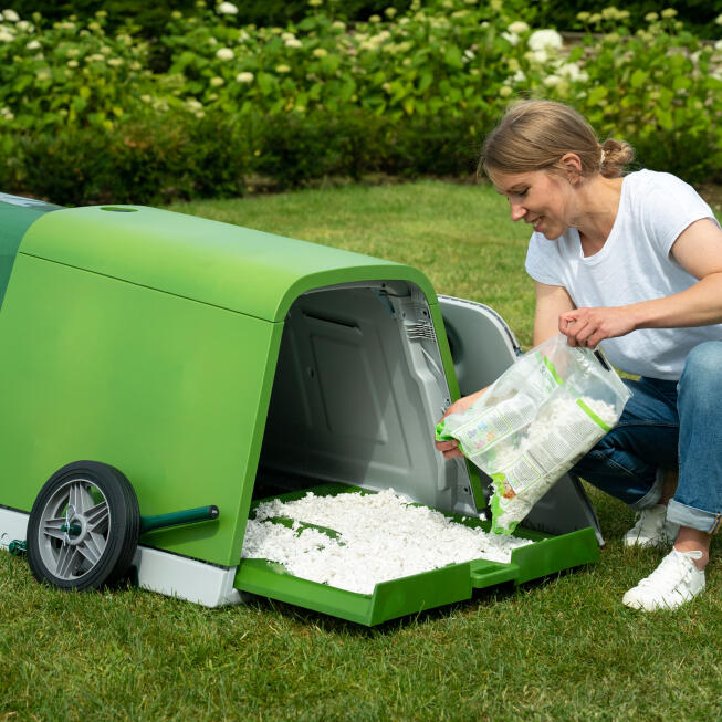 Vrouw vult de bodembak van het Eglu Go konijnenhok bij