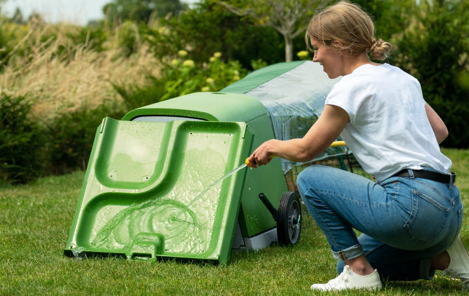 Een vrouw die haar Eglu Go hok schoonmaakt met een tuinslang.