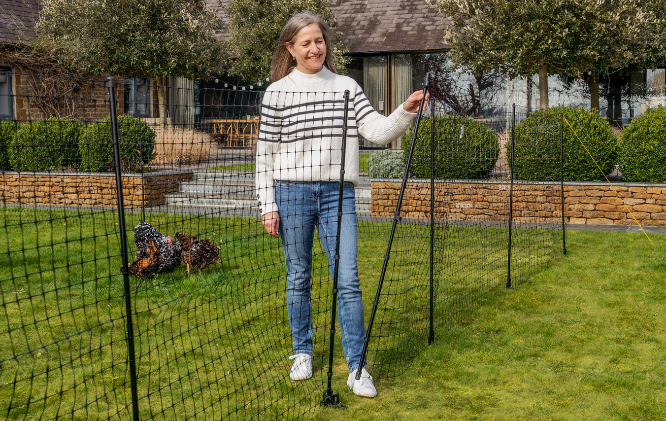 Afrastering voor kippen in tuin met vrouw die de ingebouwde toegang van Omlets afrastering voor kippen sluit