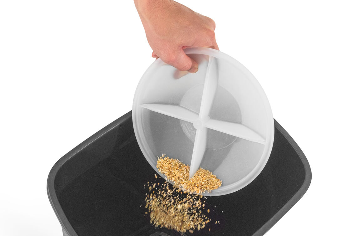 A close up of someone tipping the discarded seeds and husks collected by the innovative feeder of the Geo Bird Cage into a bin