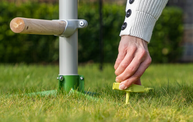 Vrouw zet vrijstaande zitstok voor kippen vast in het gras met gebruiksvriendelijke schroefharingen